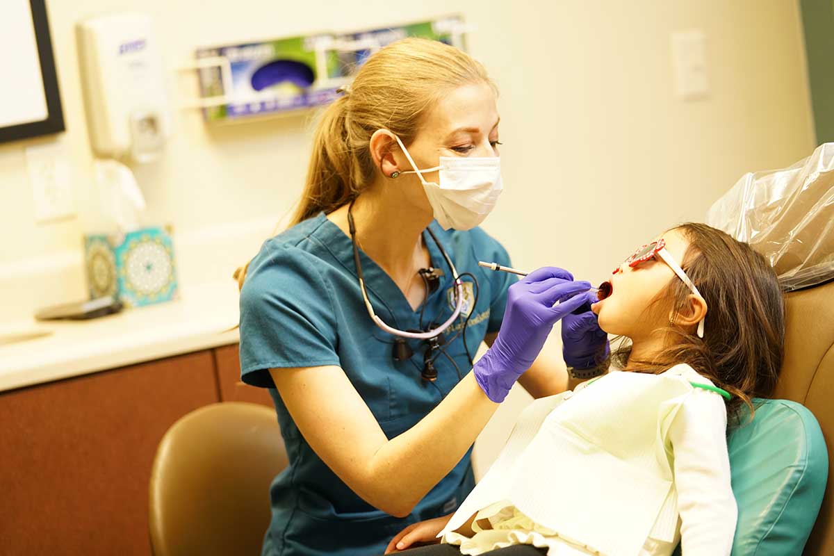 a woman dentist checking teeth of a little girl. Ivy Lane Dentistry offers periodontal maintenance services in San Antonio, TX.