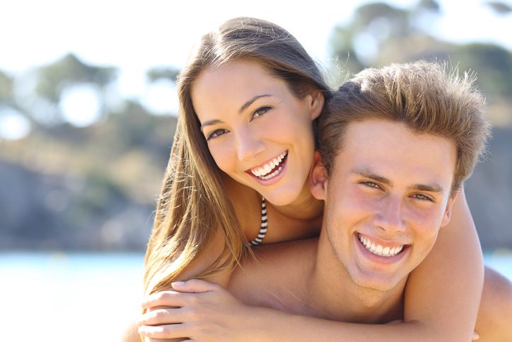 Happy couple with perfect smile and white teeth posing on the beach looking at camera. Ivy Lane Dentistry offers teeth whitening services in San Antonio, TX.