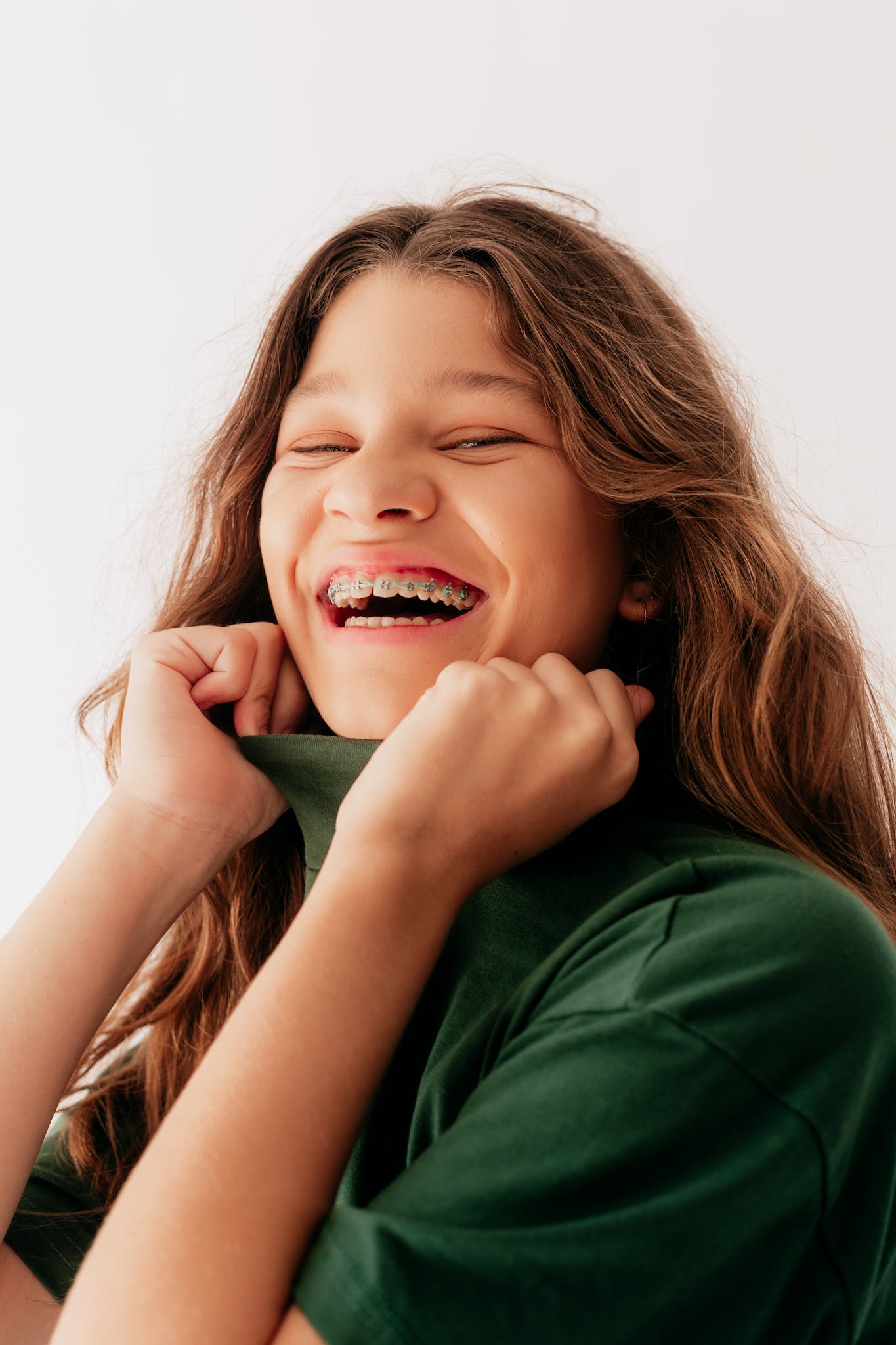 Studio Shoot of a Smiling Girl Wearing Green Polo Neck and Braces. Ivy Lane Dentistry offers multiple options for braces for teens in San Antonio, TX. 