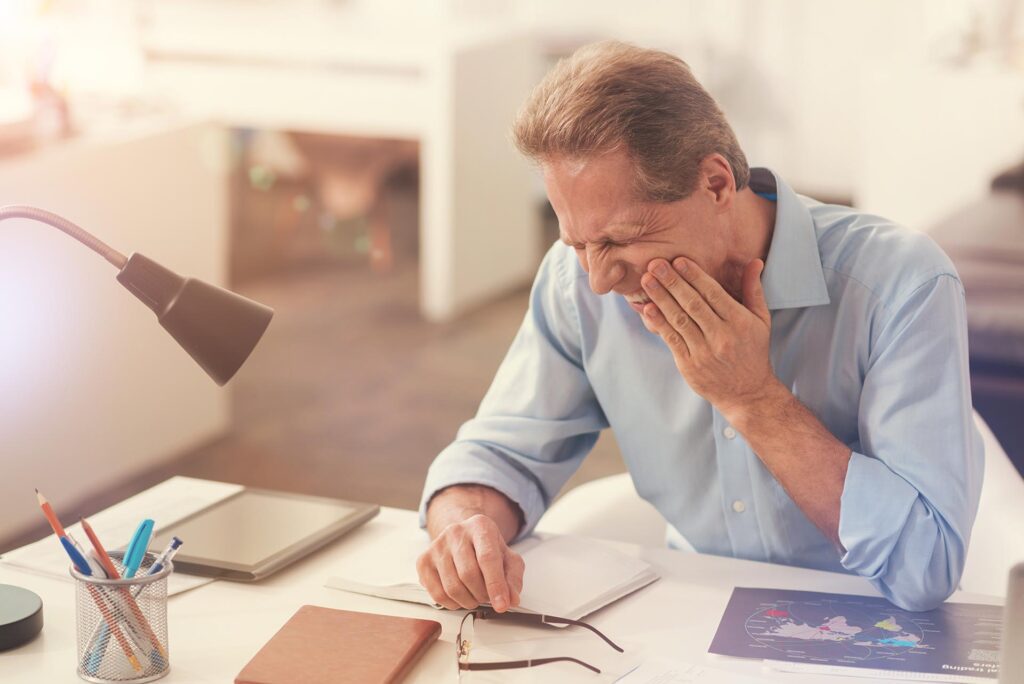 Mature, male office worker suffering from a toothache. Ivy Lane Dentistry offers advanced treatment for severe case of gum disease.